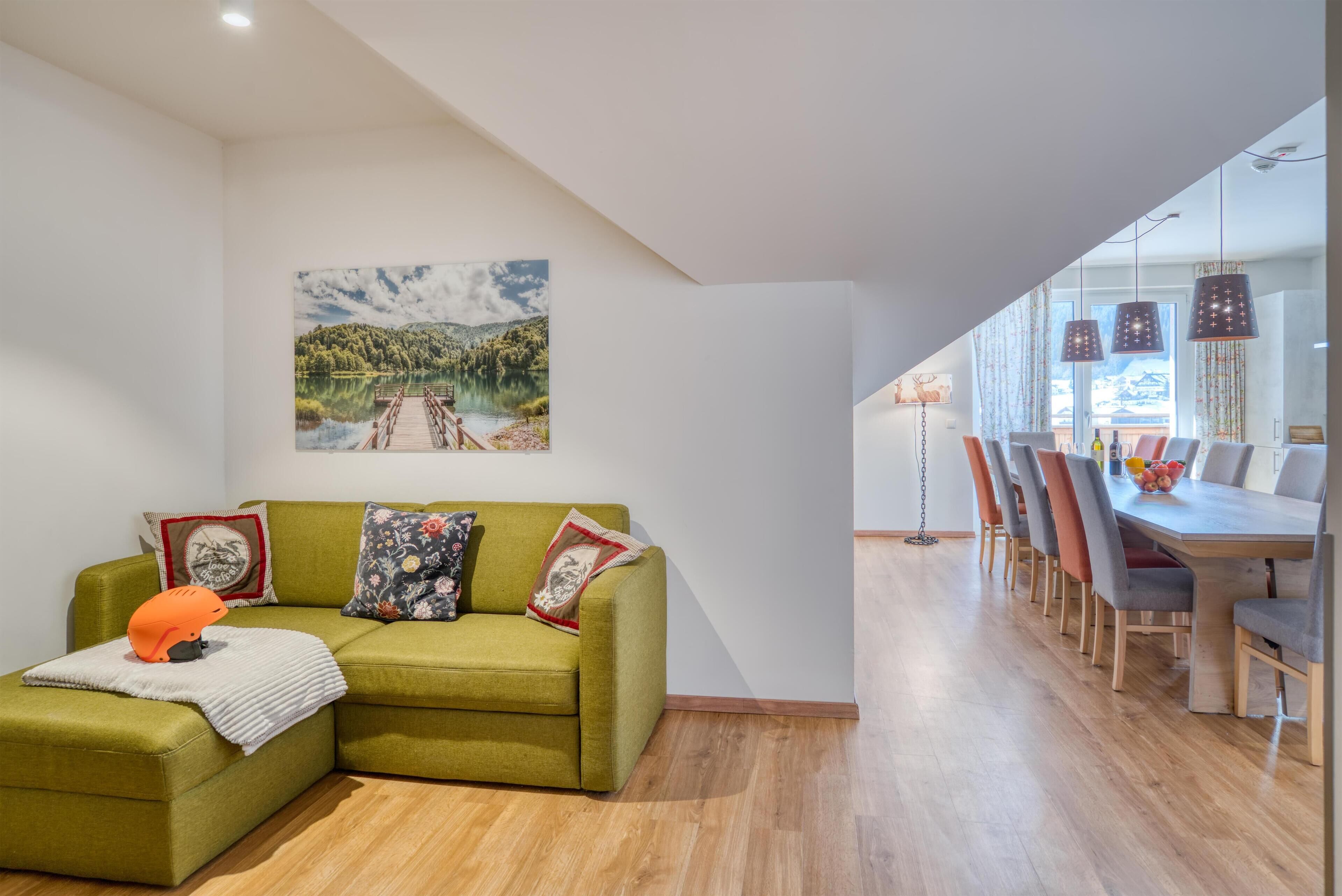 Una sala de estar moderna con un sofá verde, una mesita con un objeto naranja y un cuadro de un lago y un puente.
