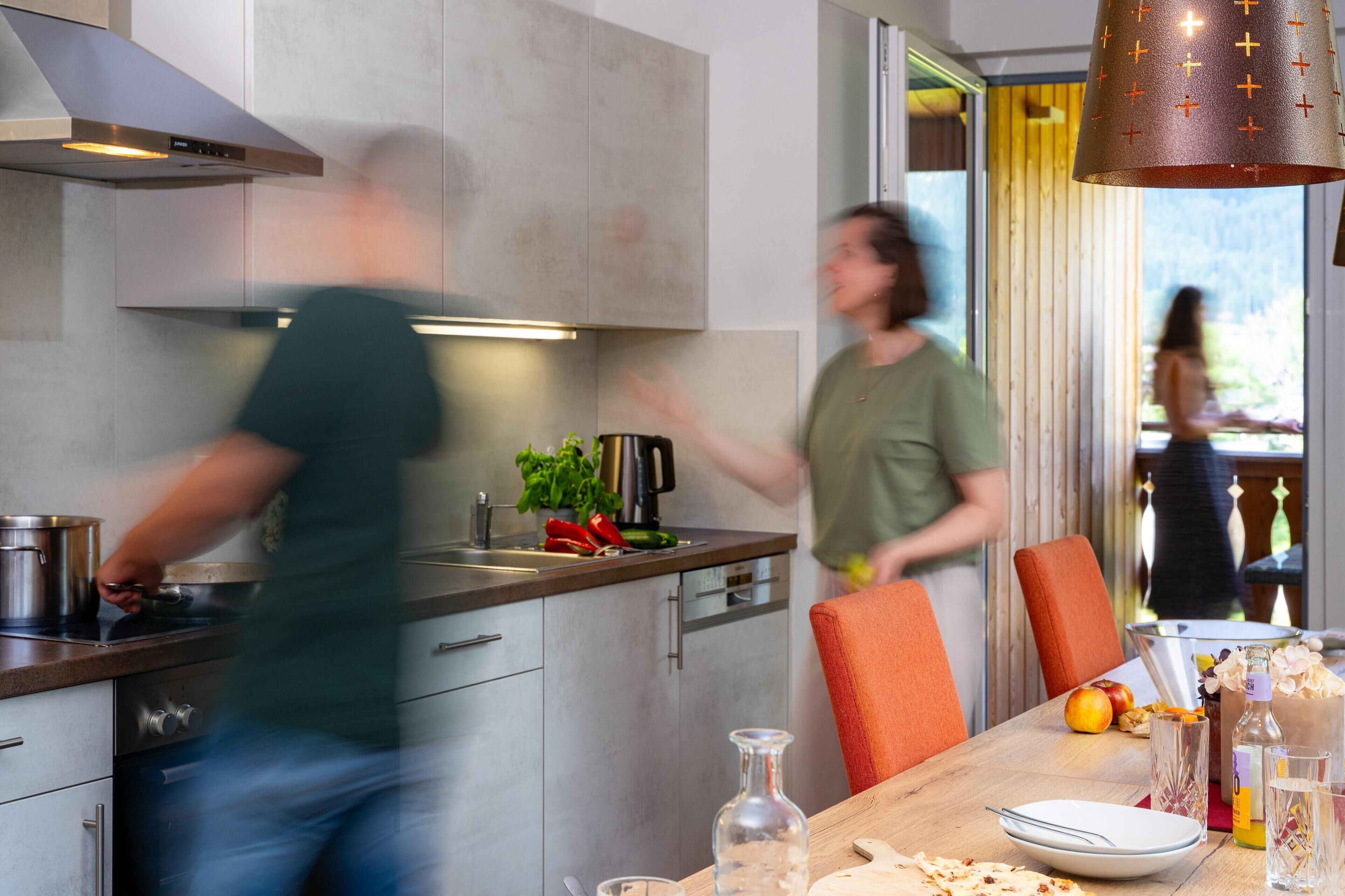 Une cuisine moderne dotée d’appareils électroménagers en acier inoxydable, un coin repas avec une table dressée pour deux personnes, et une vue sur l’extérieur par le biais d’une fenêtre.