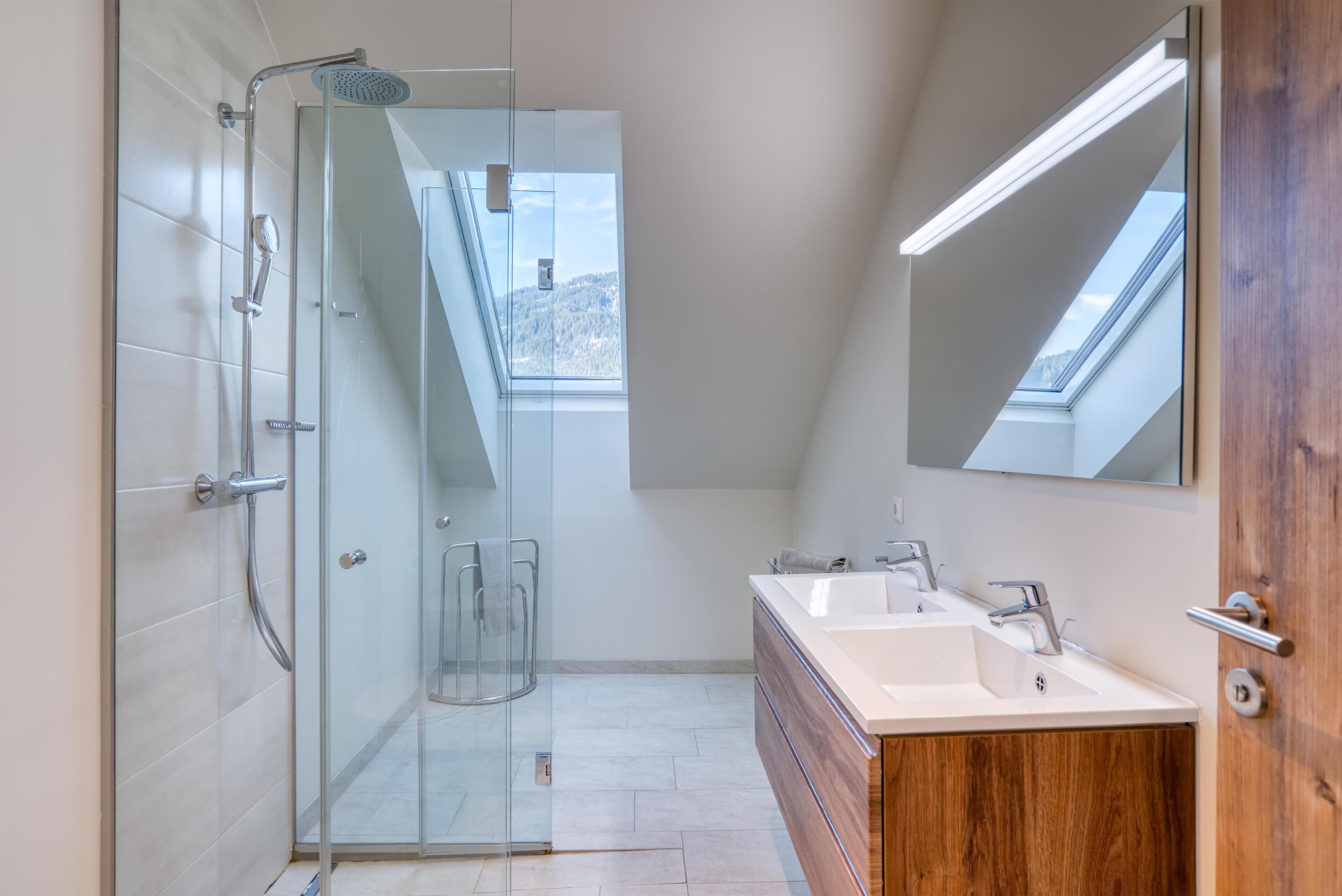 A modern bathroom with a glass shower enclosure, a skylight, and a wooden vanity with a mirror.