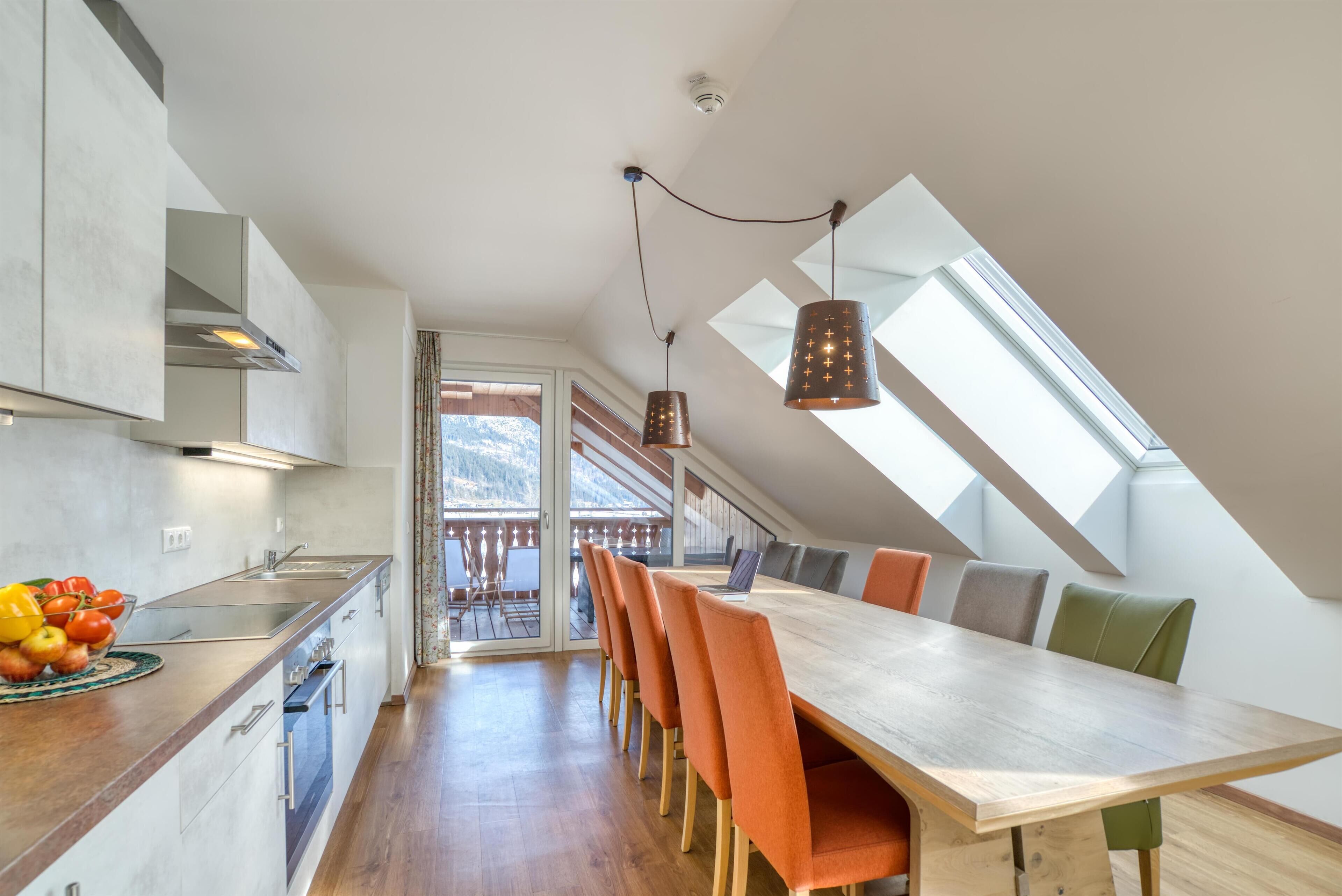 Una cocina moderna con encimera de madera, un lavamanos integrado y una zona de comedor con una mesa larga y sillas coloridas.