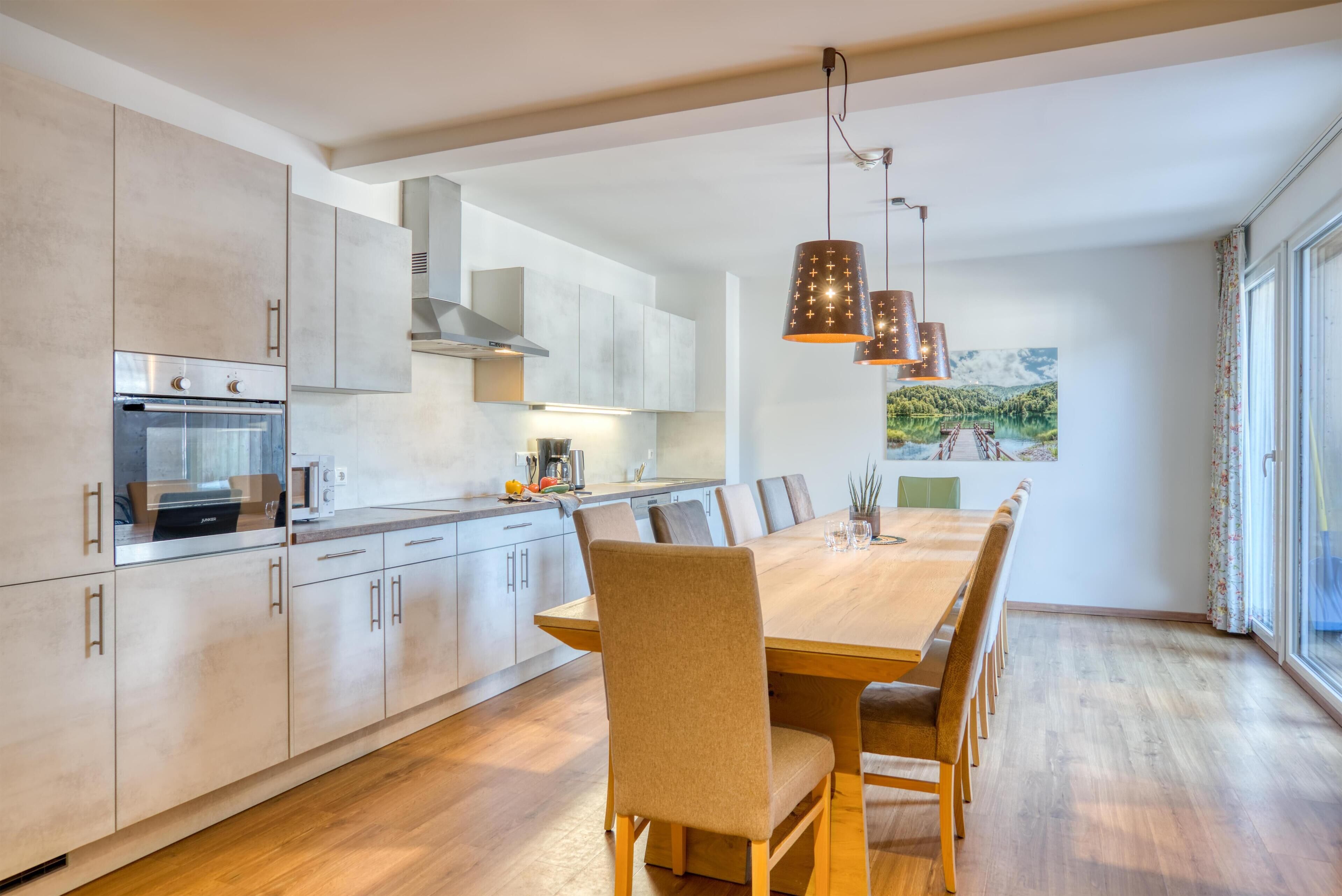 Una cocina moderna con una gran mesa de comedor, electrodomésticos integrados e iluminación colgante.