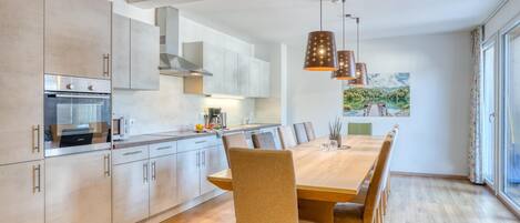 A modern kitchen with a large dining table, built-in appliances, and pendant lighting.