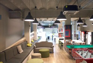 A modern lounge area with sofas, ottomans, and a foosball table. - Hola Hostal Eixample - Hostel (Barcelona)