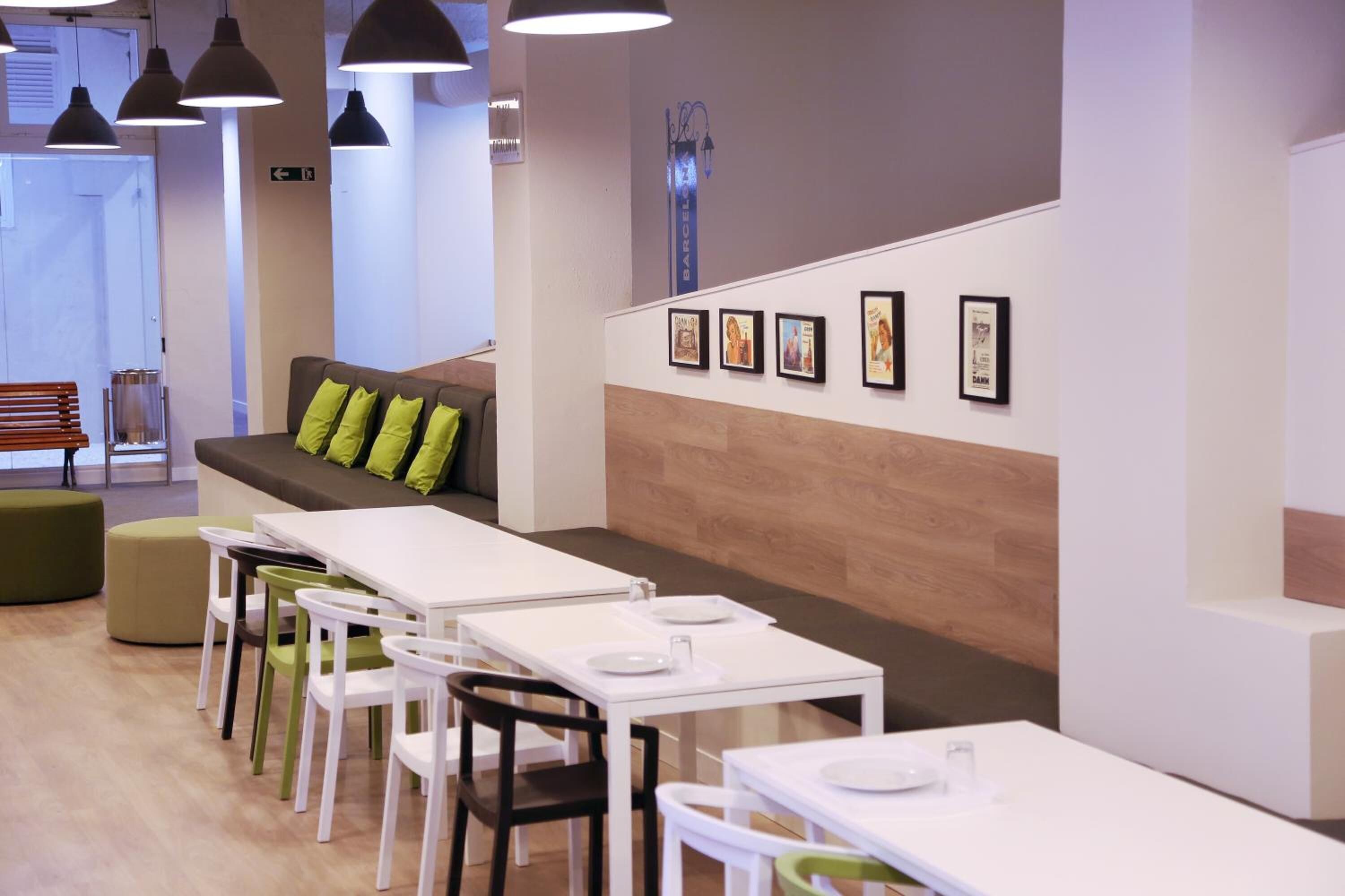 Un comedor moderno con mesas y sillas blancas, un banco acolchado verde y cuadros en la pared.