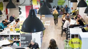 Um espaço de refeições interno movimentado, com várias mesas e luminárias pendentes pretas.