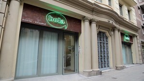 Um edifício com letreiro de neon que diz "hola" e "HOSTAL / EXAMPLE", indicando uma pensão.