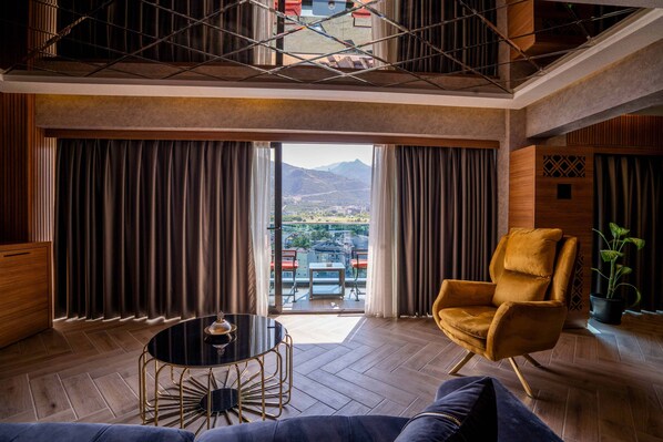 A modern hotel room with a large window, a round table, a sofa, and a yellow armchair.