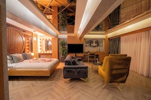 A spacious room with a bed, a sofa, a TV, and a dining area.