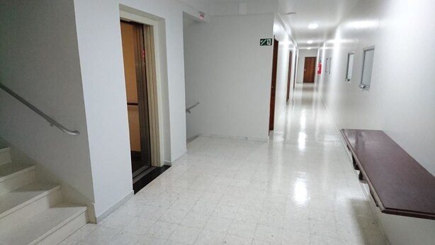 A clean, well-lit hallway with a staircase on the left, a bench on the right, and doors leading to other areas.