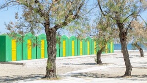 A row of green and yellow beach huts with a sandy beach and trees in the foreground. - Centro Vacanze Lido Smeraldo (Lecce)