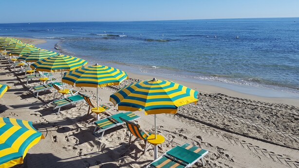 A beach with rows of striped beach umbrellas and lounge chairs. - Centro Vacanze Lido Smeraldo (Lecce)
