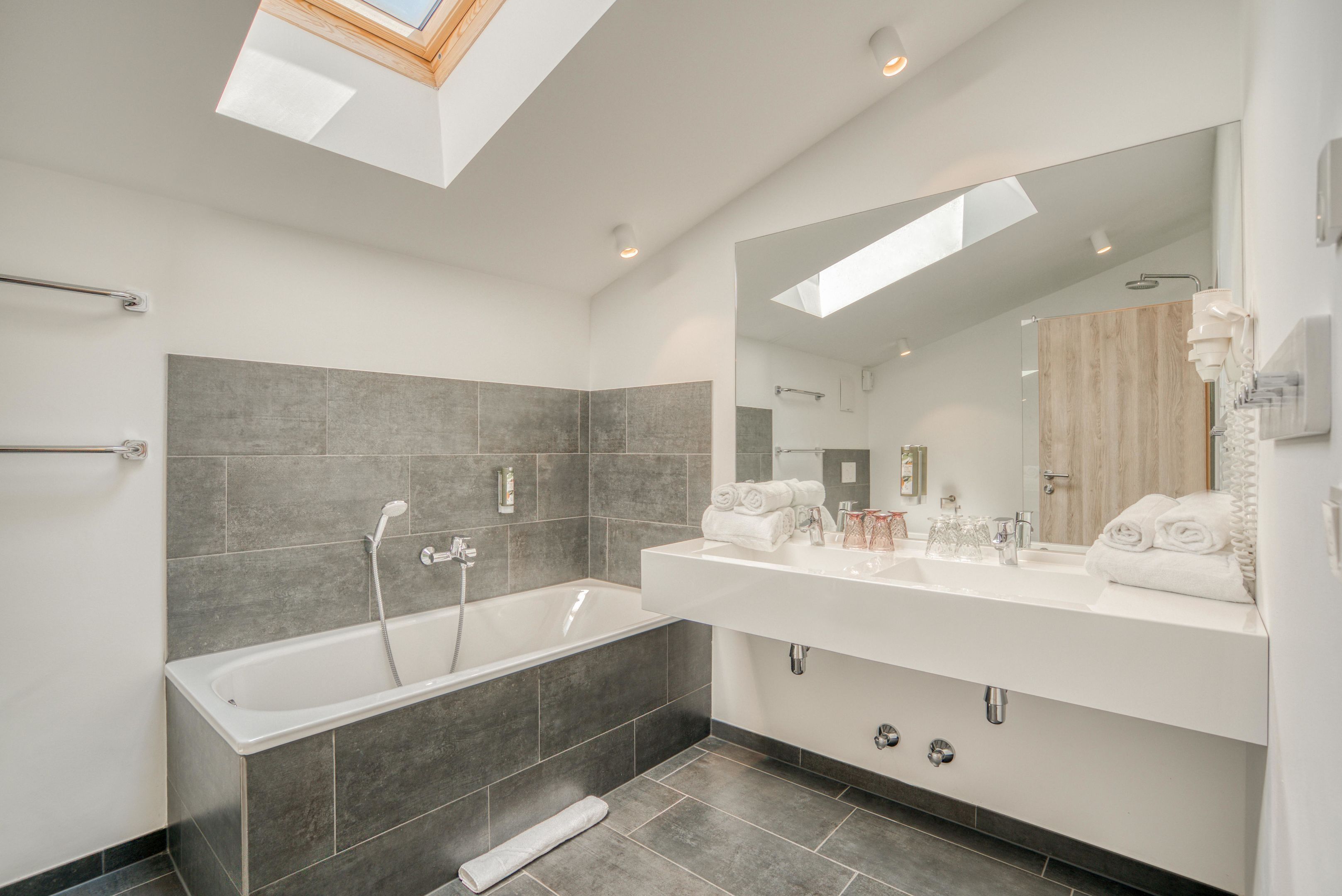A modern bathroom with a bathtub, a large mirror, and a skylight.