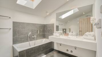 A modern bathroom with a bathtub, a large mirror, and a skylight.