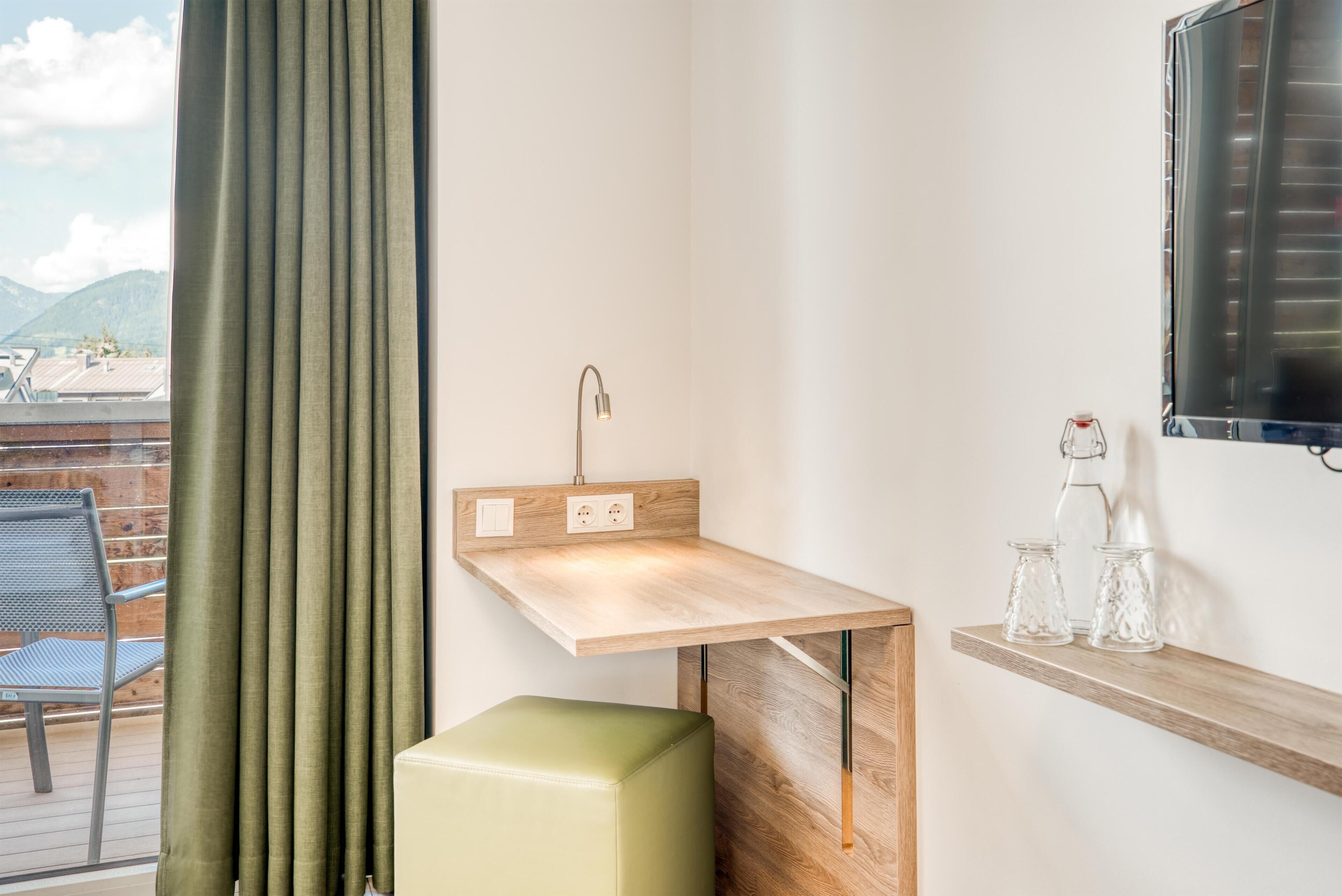 A small bathroom with a wooden vanity, a green stool, and a shelf with glass jars.