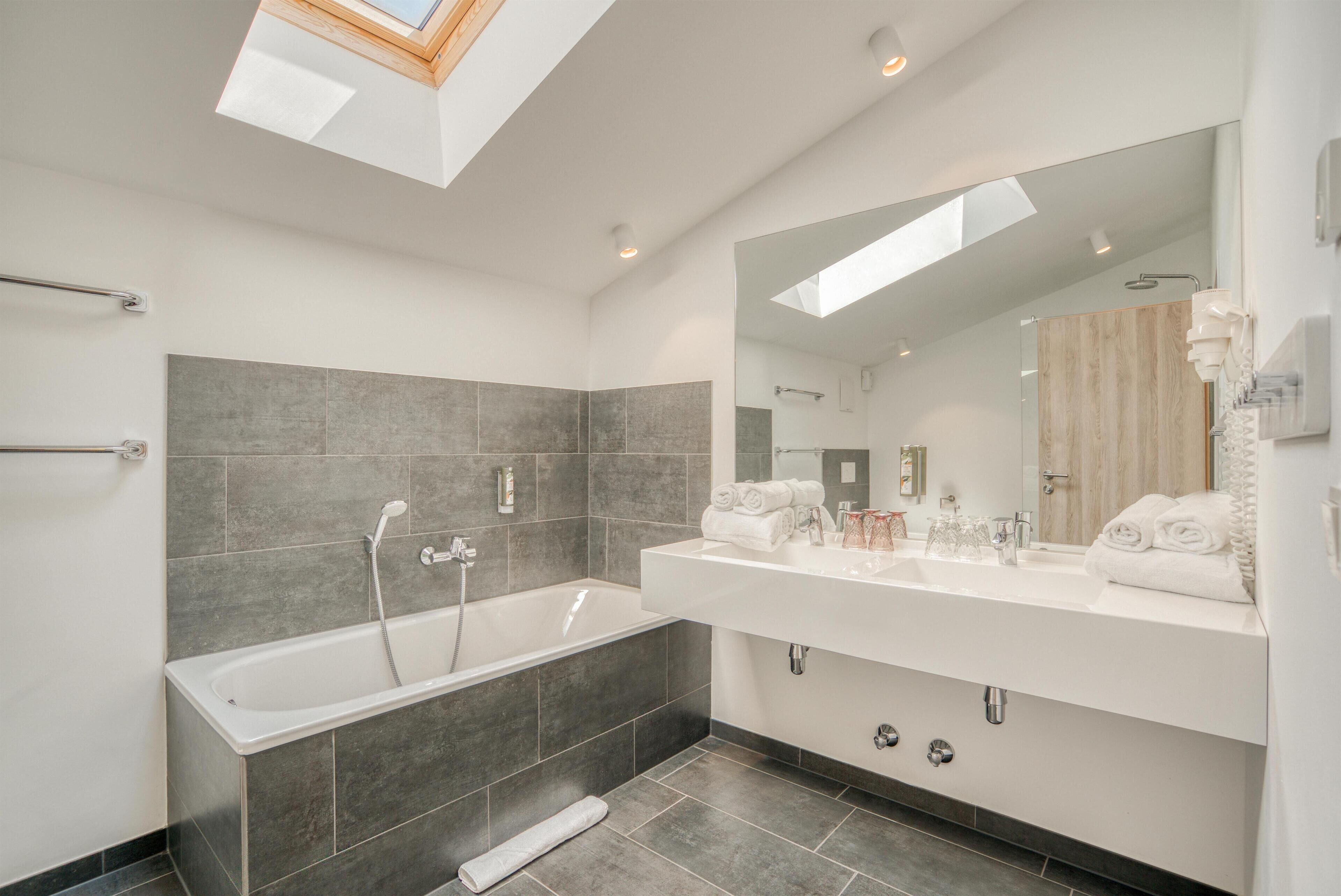 A modern bathroom with a freestanding bathtub, a large mirror, and a skylight.