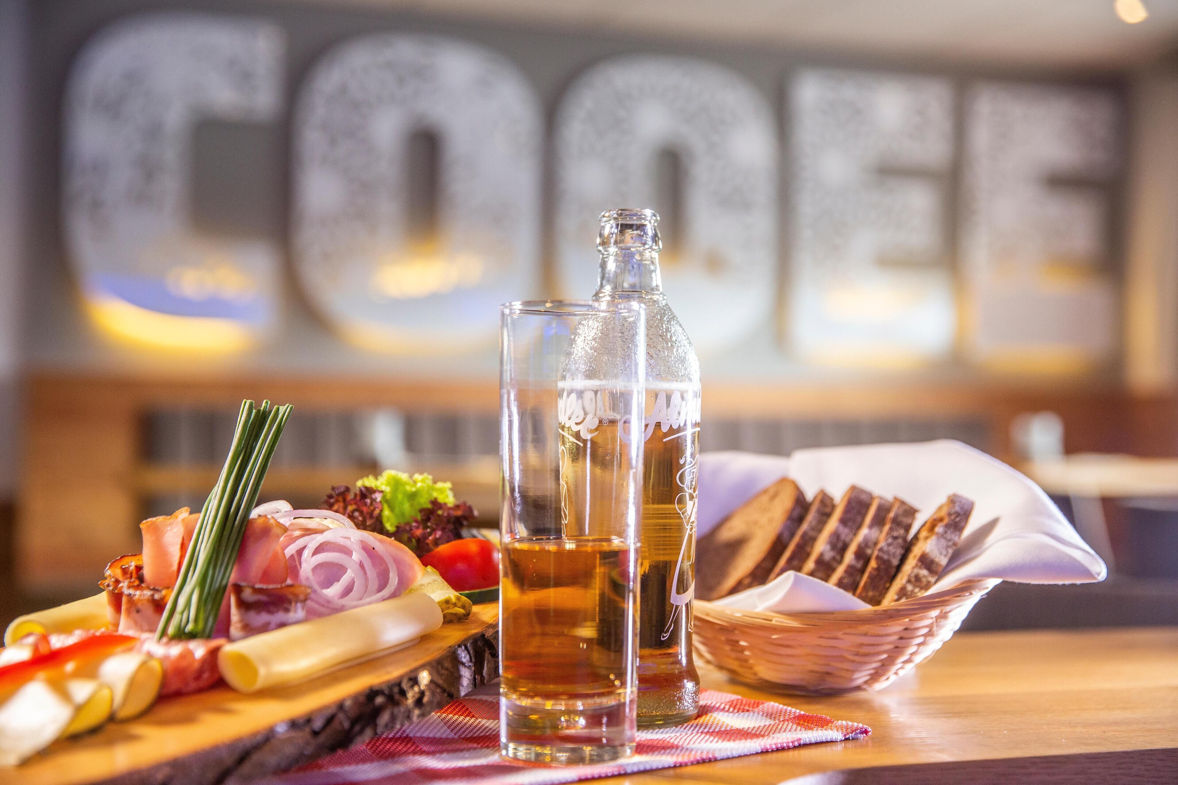 A wooden table with a charcuterie board, two bottles of beer, and a basket of bread.