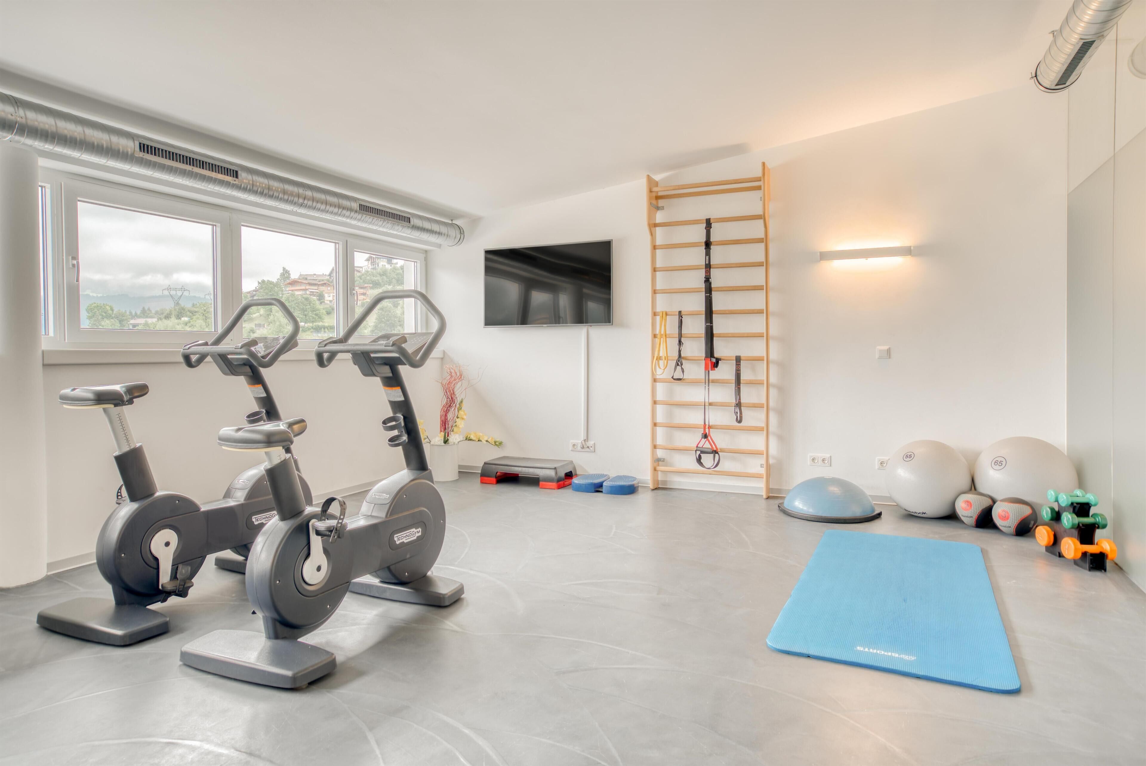 Une salle de sport équipée de vélos d’appartement, d’un tapis bleu, de ballons d’exercice et d’un téléviseur fixé au mur.