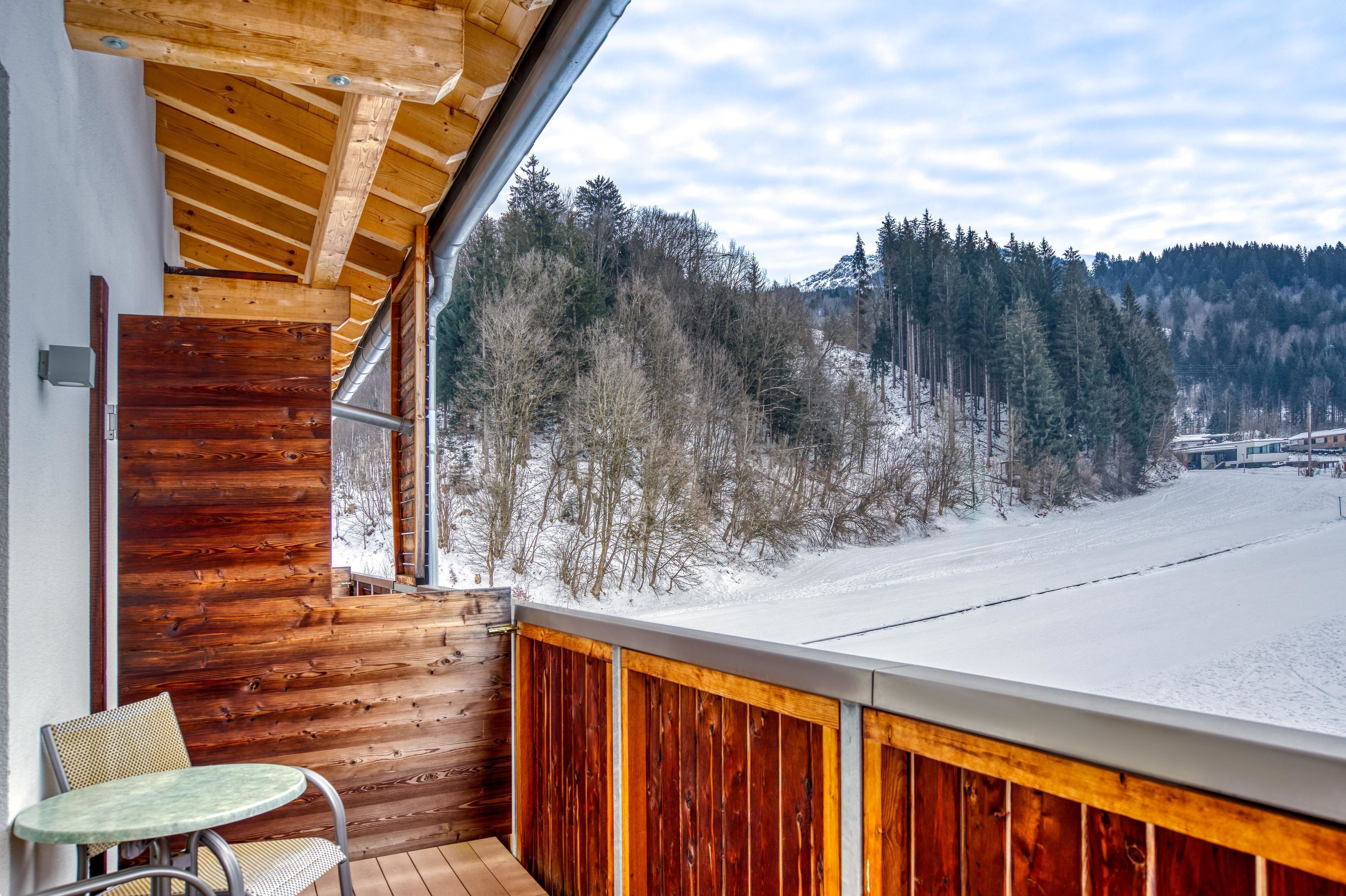 A wooden balcony with a view of a snow-covered landscape and trees.