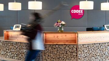Un mostrador de recepción de diseño de madera, un jarrón con flores y un letrero que dice 'COOEE'.