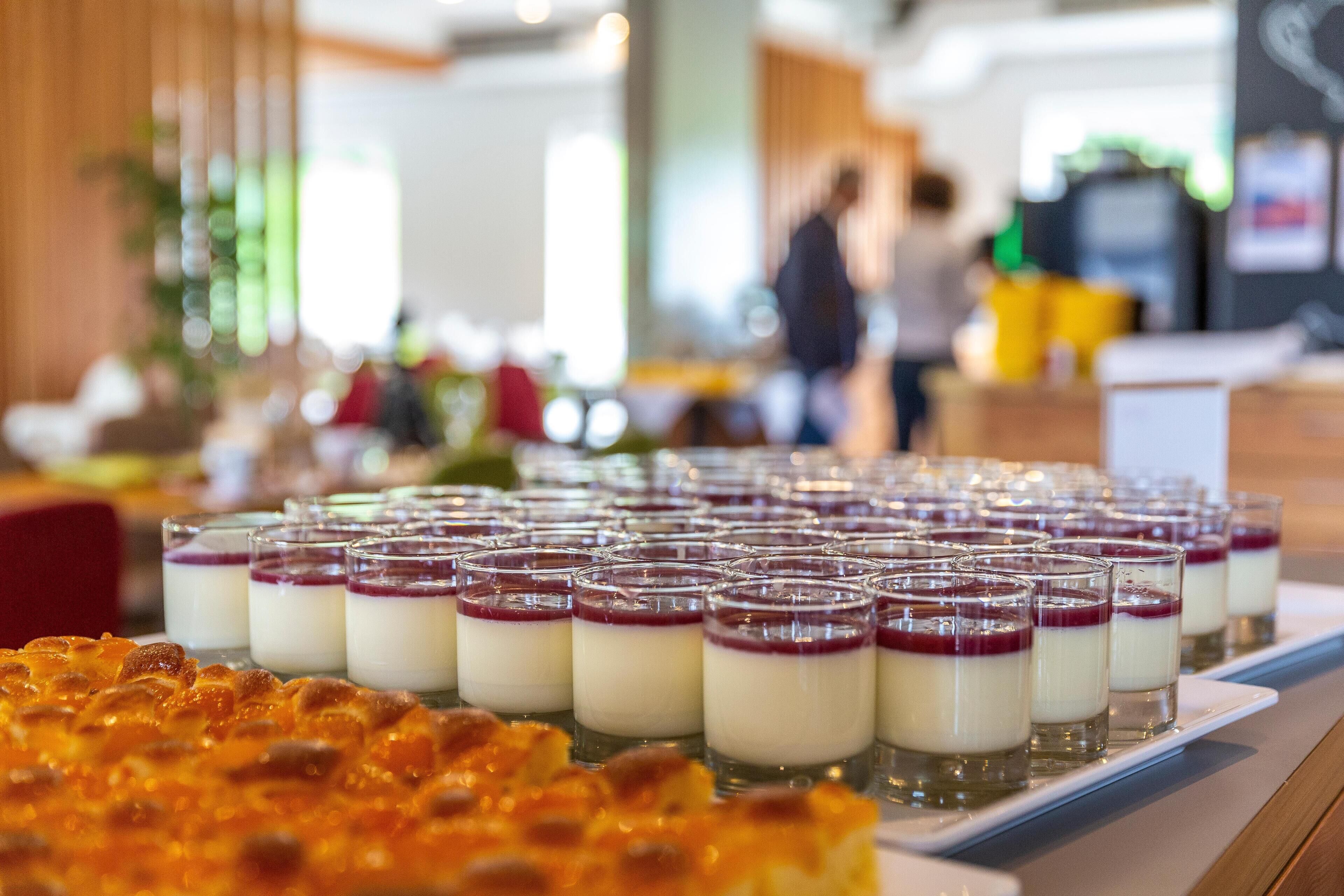 A dessert buffet with small glass servings of layered dessert and a pizza.