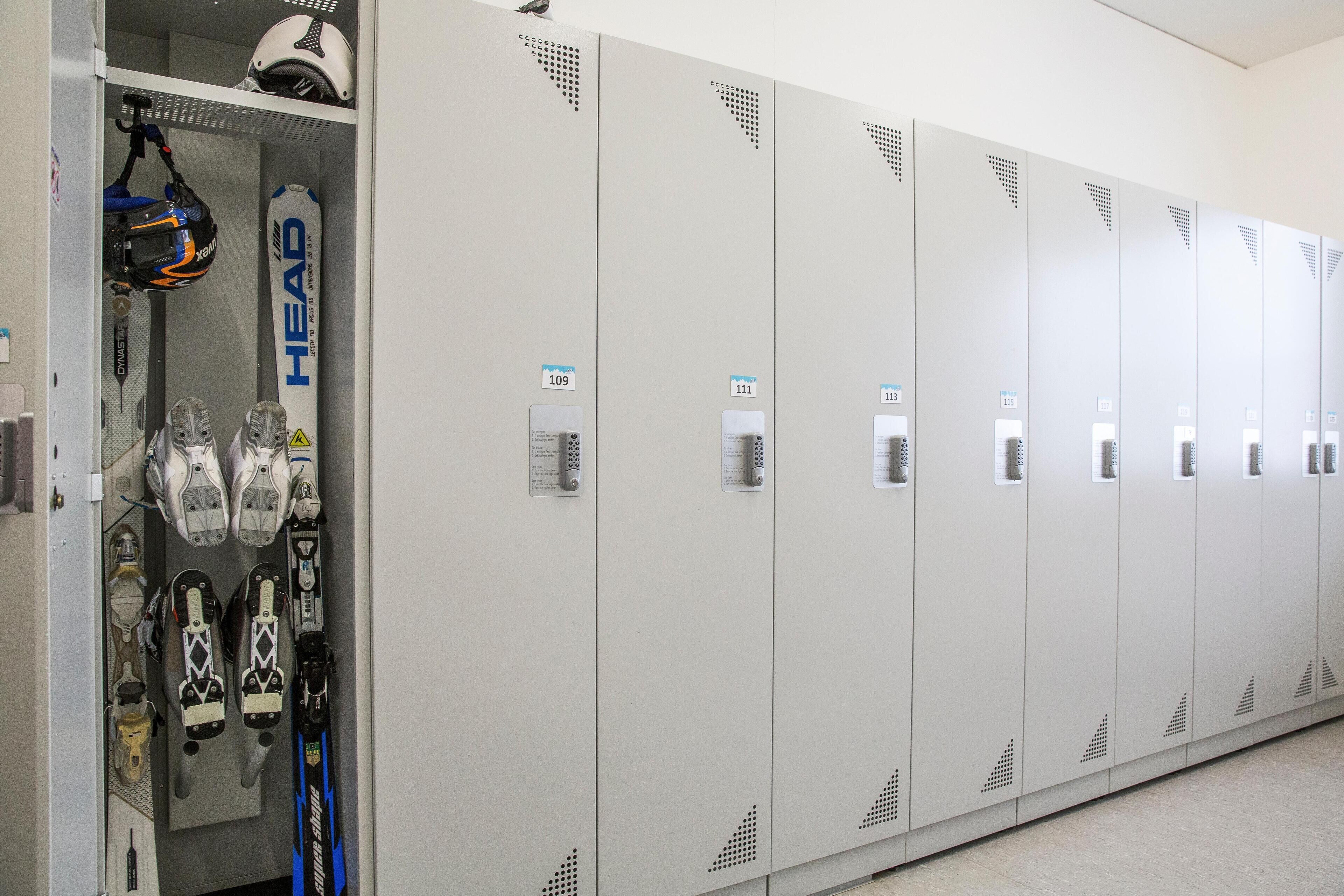 A row of lockers with numbered tags, a helmet, and skis leaning against the lockers.