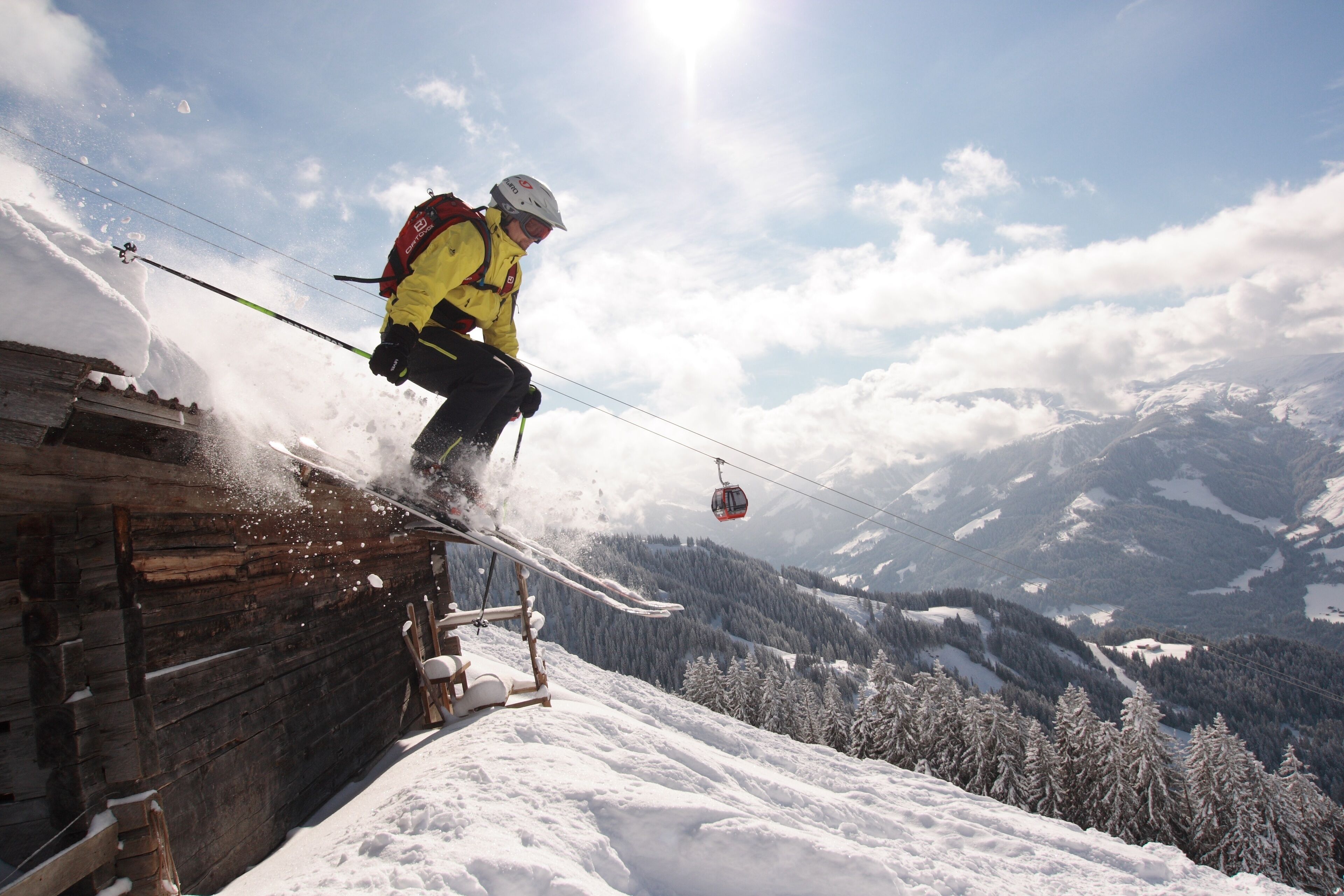 A person snowboarding on a wooden structure with a ski lift in the background and a mountainous landscape.