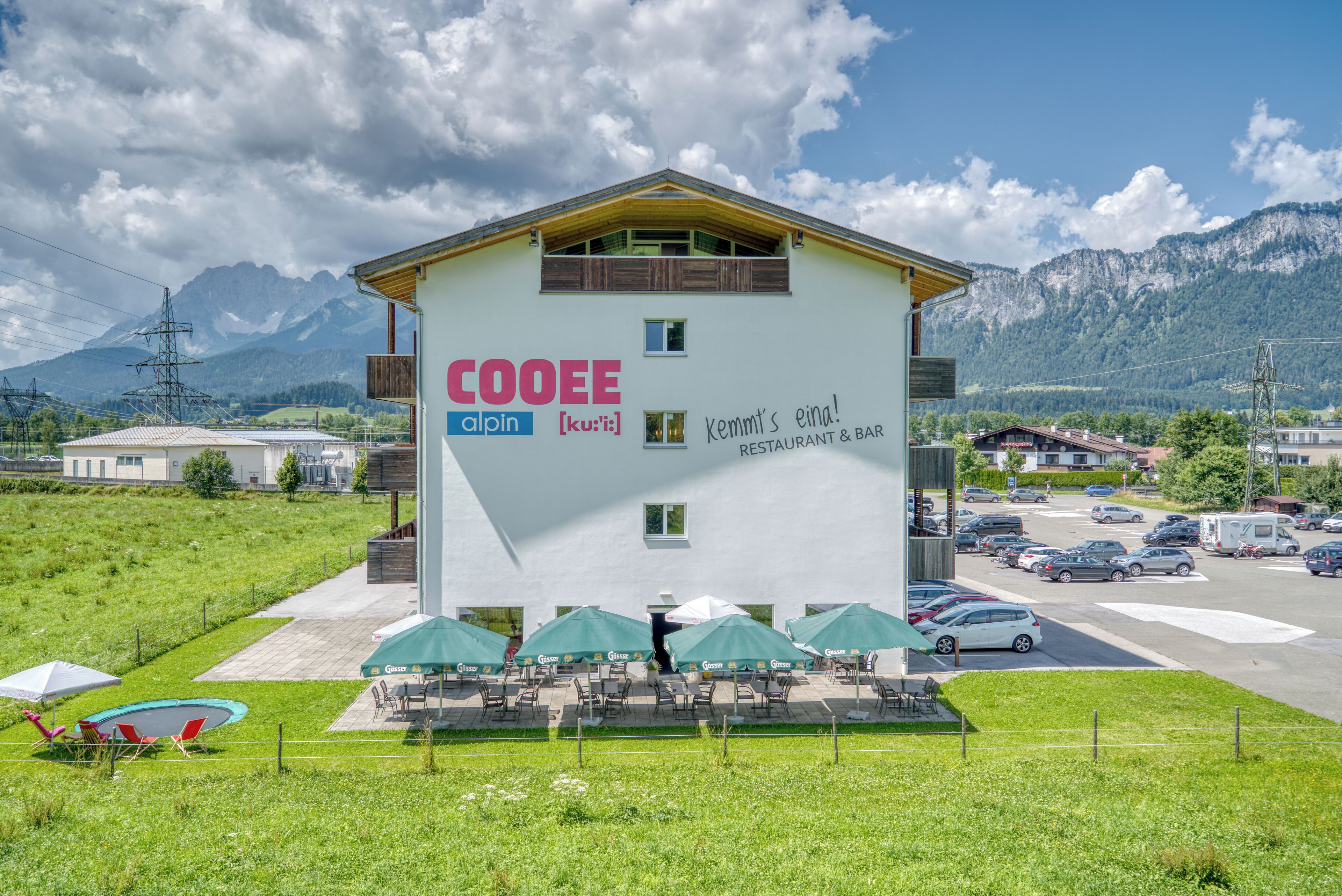 A building with outdoor seating and a sign for 'COOEE alpin [ku:ti] RESTAURANT & BAR'.