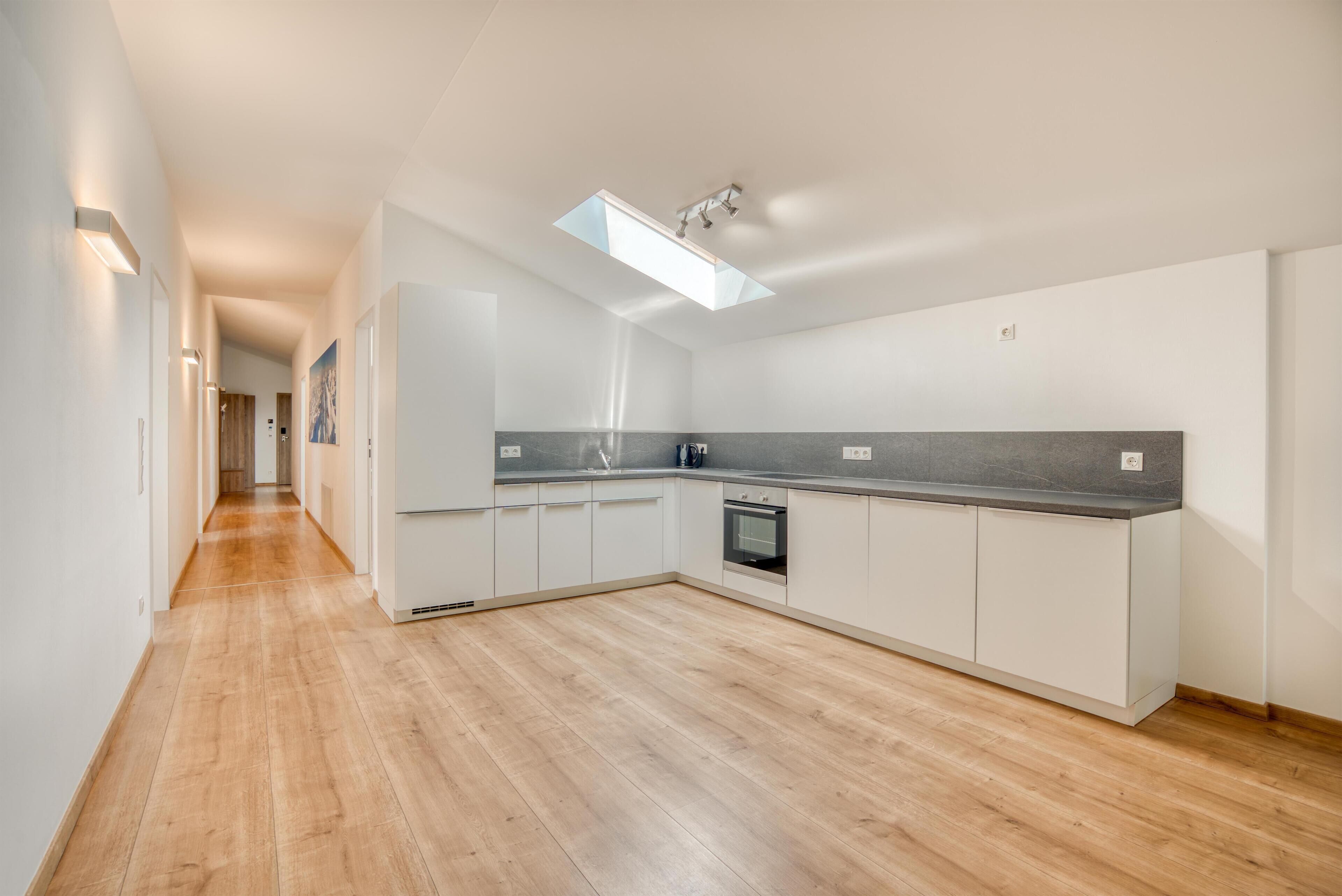 A modern kitchen with white cabinetry, a built-in oven, and a skylight.