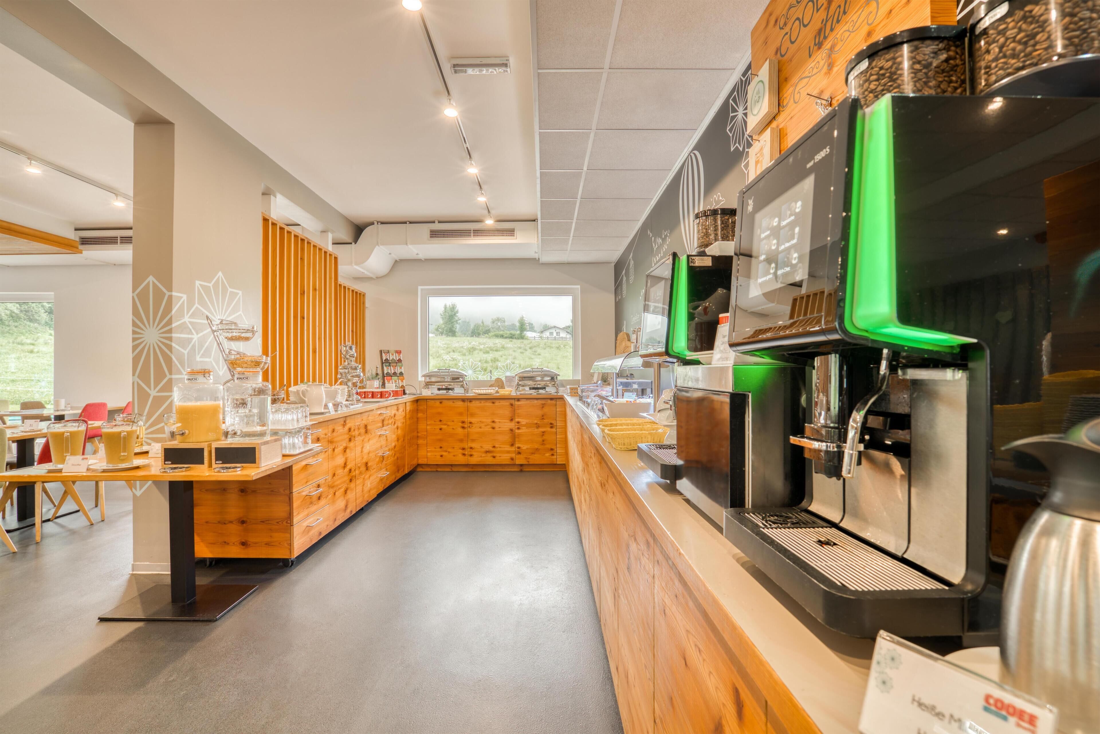 Una cafetería moderna con mostrador de madera, máquinas de café y vistas al exterior.