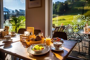 A breakfast table with a basket of bread, a bowl of fruit, a glass of orange juice, and a cup of coffee.