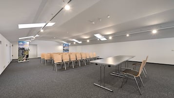 A conference room with a long table and chairs, ceiling lights, and a carpeted floor.