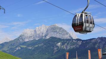 A cable car with "St. Johann" branding, a mountainous backdrop, and flags with "St. Johann" text.