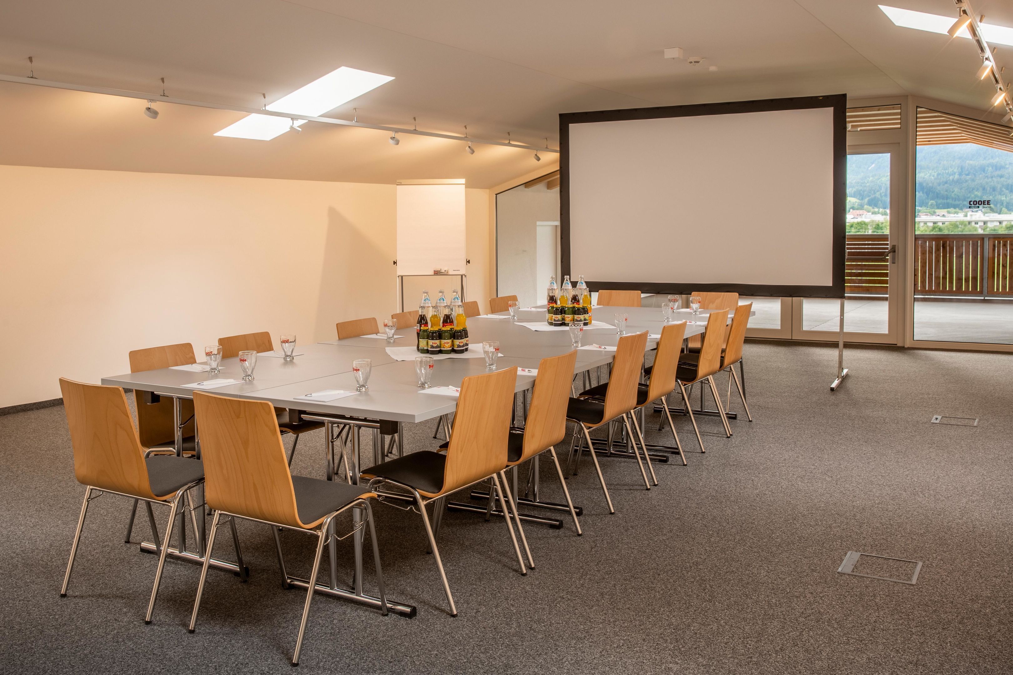 Une salle de conférence équipée d’une longue table, de chaises, d’un écran de projection et offrant une vue sur l’extérieur.