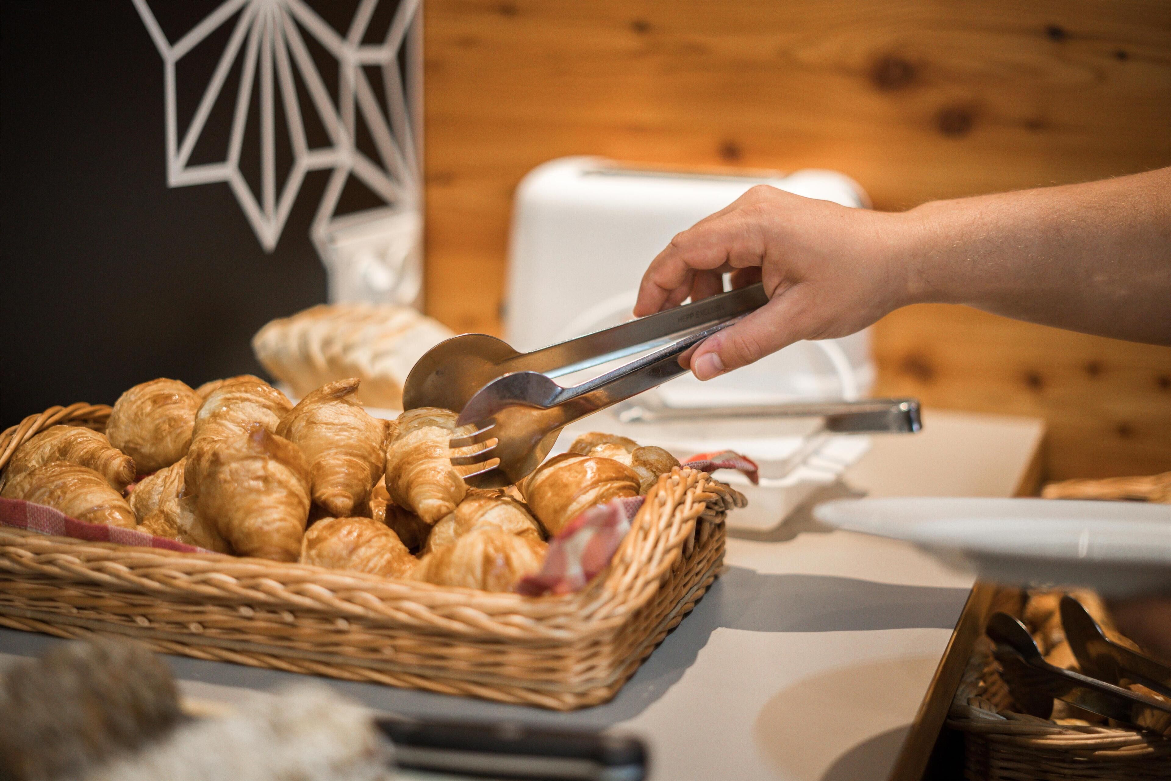 Une main utilisant des pinces pour prendre un croissant dans un panier.