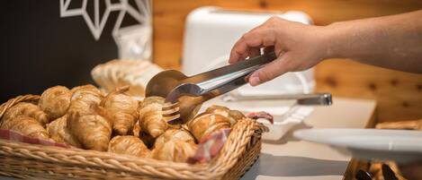 Une main utilisant des pinces pour prendre un croissant dans un panier.