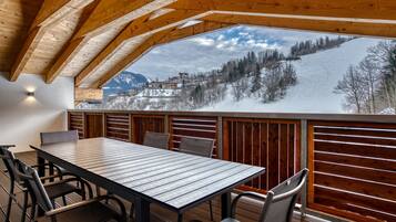Eine Holzterrasse mit Tisch und Stühlen, mit Blick auf eine verschneite Berglandschaft.