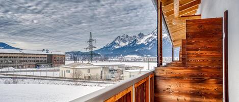 A wooden balcony with a view of snow-covered mountains and a cityscape.