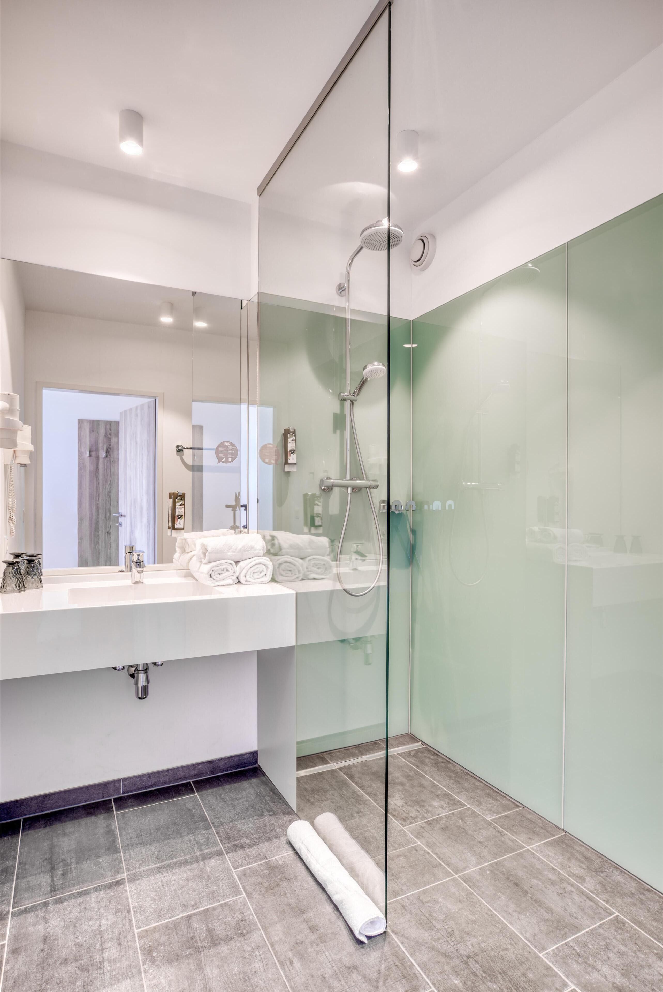 A modern bathroom with a glass shower enclosure, a white sink with a mirror, and neatly rolled towels.