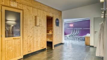 Een sauna met houten wanden en een glazen deur, een handdoekhouder en een bordje met de functie van de ruimte.