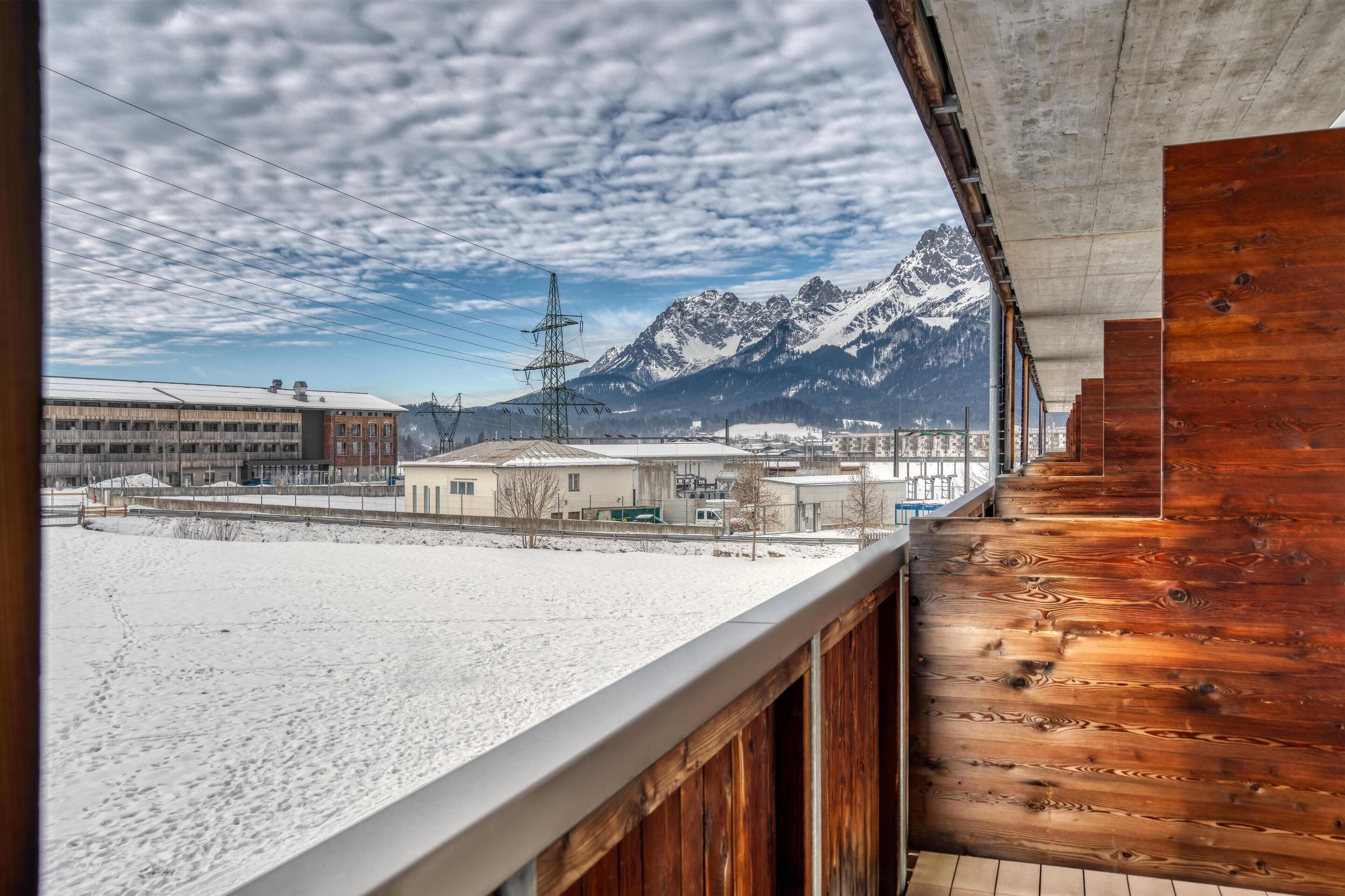 A snowy landscape with a mountain in the background, a building with a flat roof, and a wooden balcony.