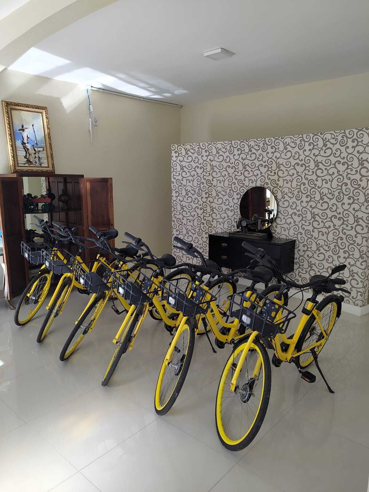 Una stanza con una fila di biciclette gialle appoggiate a una parete decorata, un mobiletto in legno e un quadro appeso al muro.