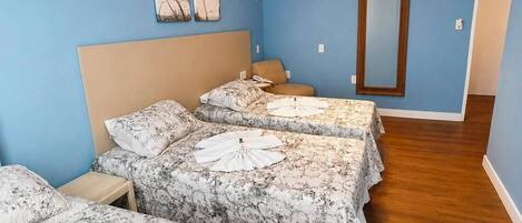 Ein Hotelzimmer mit einem großen Bett, einem kleineren Bett, einem Nachttisch, einem Spiegel und einer Deckenleuchte.
