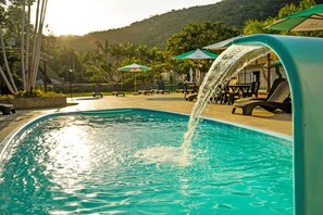 A swimming pool with a water feature, surrounded by lounge chairs and umbrellas. - Hotel Sandrini (Tubarao)