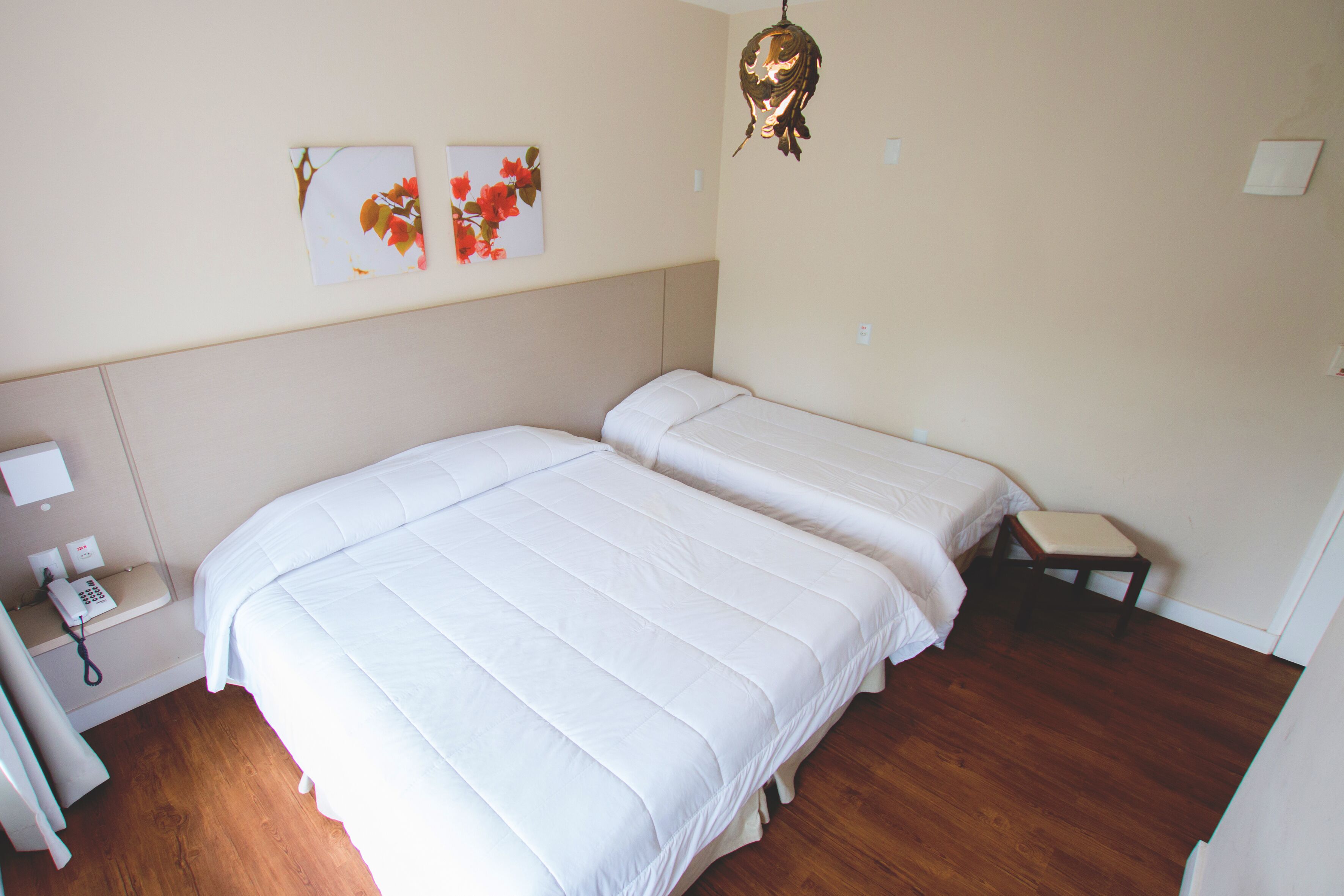 A bedroom with two beds, a bedside table with a lamp, and a wall-mounted telephone.