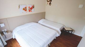 A bedroom with two beds, a bedside table with a lamp, and a wall-mounted telephone.