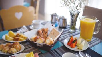 A breakfast table with croissants, pastries, fruit, and a pitcher of orange juice.
