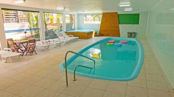 Ein Innenpool mit Holzterrasse, Liegestühlen und einem Whirlpool.
