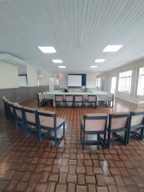 Un salón de conferencias con una larga mesa, sillas y una pantalla de proyector.