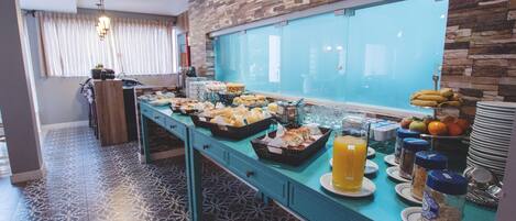 Un bufé de desayuno con diversas opciones de comida y bebidas, una pared de madera y baldosas de piso estampadas.