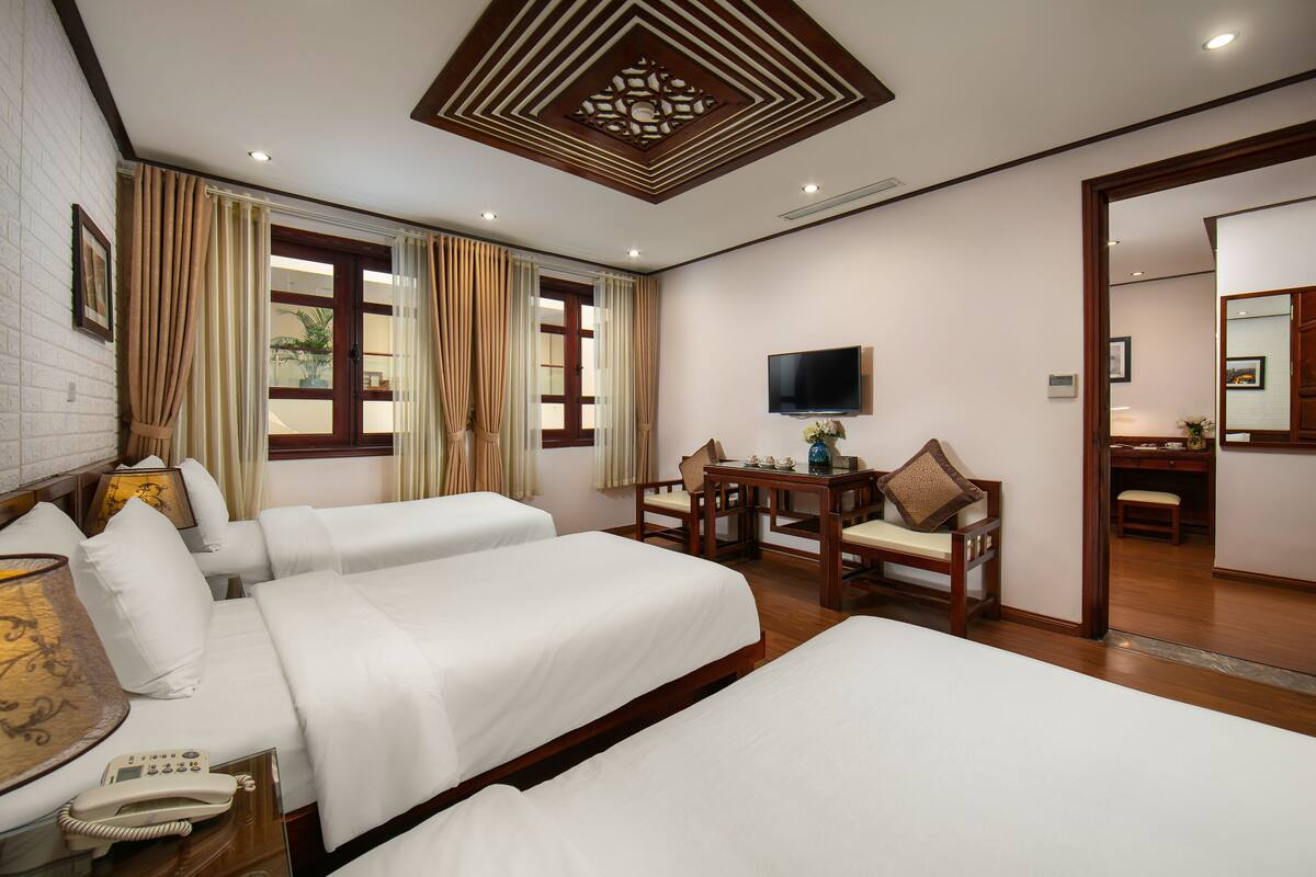 A hotel room with two beds, a desk, a chair, a TV, and a bathroom visible through an open door.